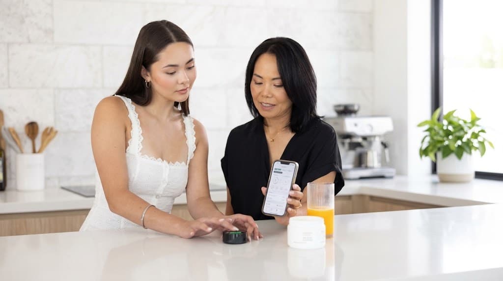 Two people reviewing a Prysm iO wellness score on a phone beside the scanner