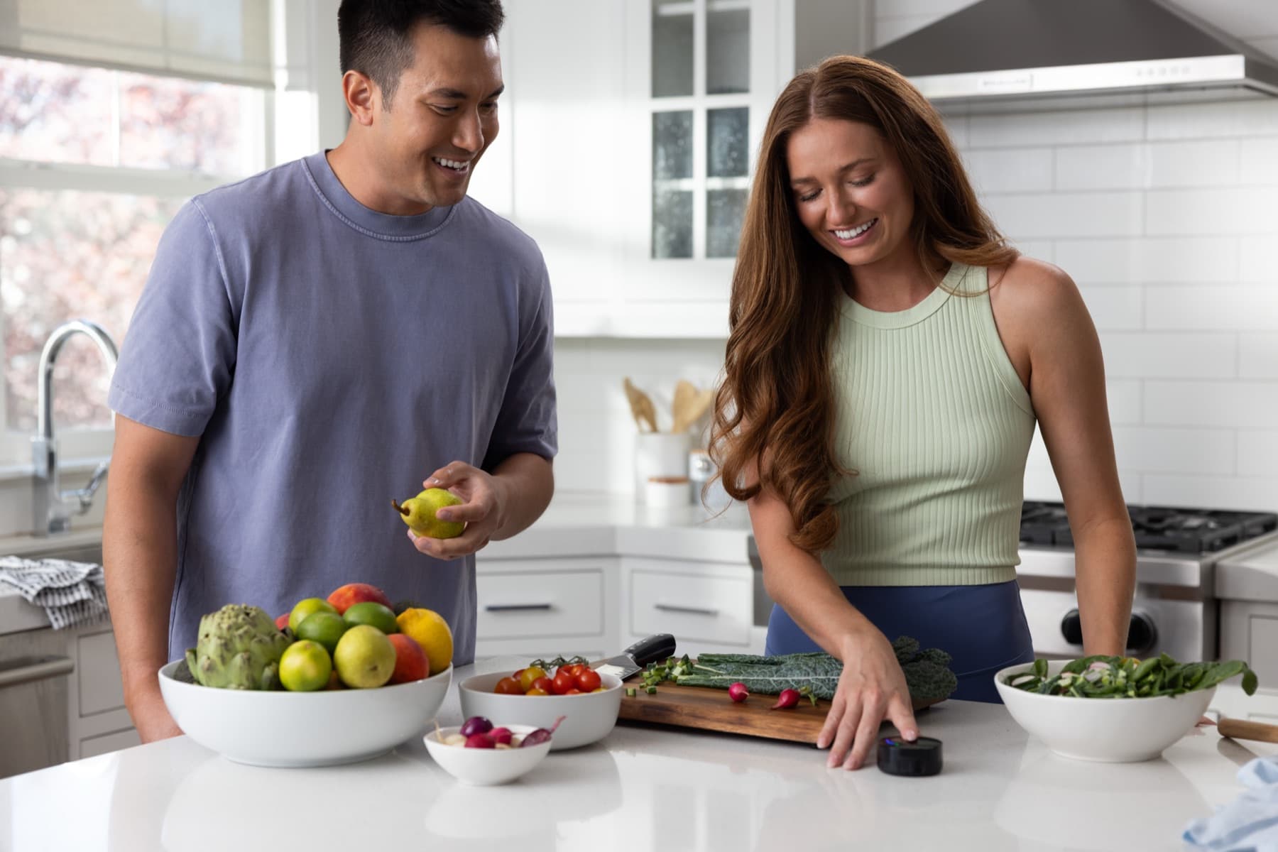 A couple laughing over a bowl of fresh fruit and vegetables as one of them touches the Prysm iO scanner on the kitchen counter